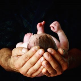 Newborn baby held by father in his cupped hands