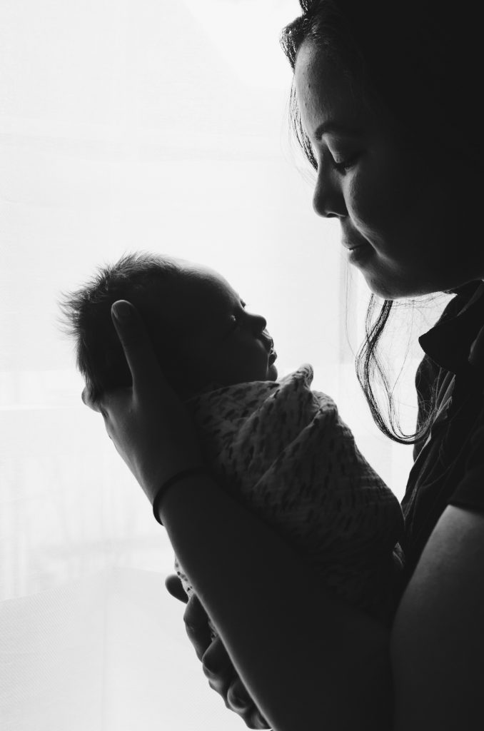 Asian mother looks lovingly at her newborn swaddled baby. Black and white image